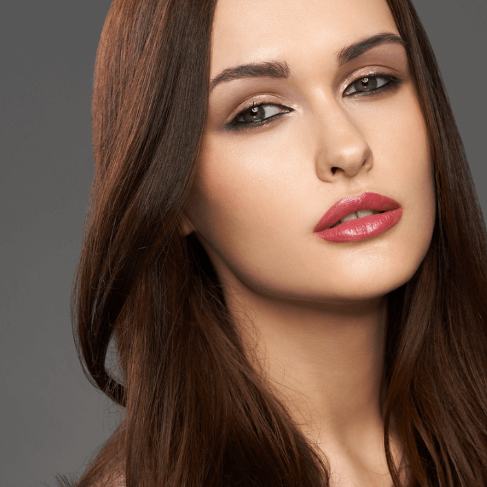 Portrait of a model with long brown hair and glamorous makeup, emphasizing smooth skin and bold lips.