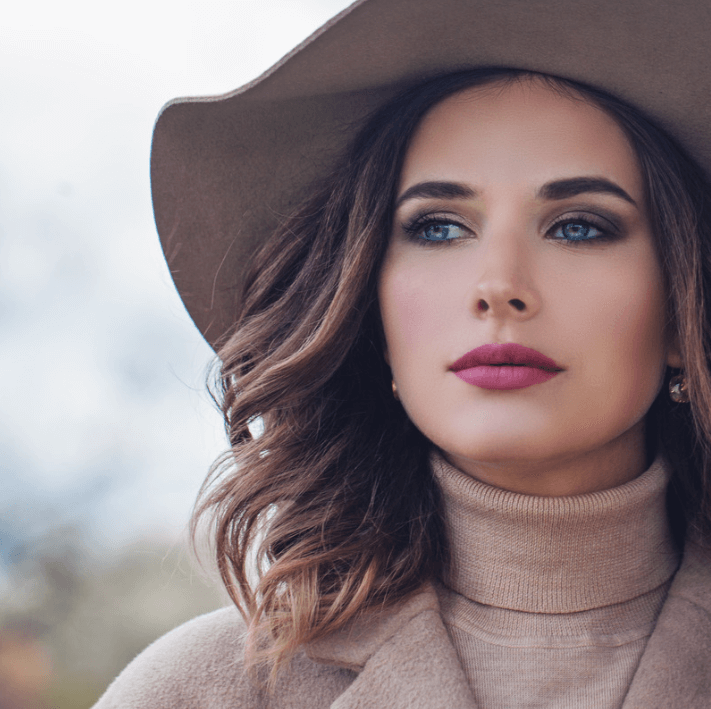 Portrait d'une femme stylée portant un chapeau et mettant en valeur ses lèvres avec l'Huile essence soin des lèvres.