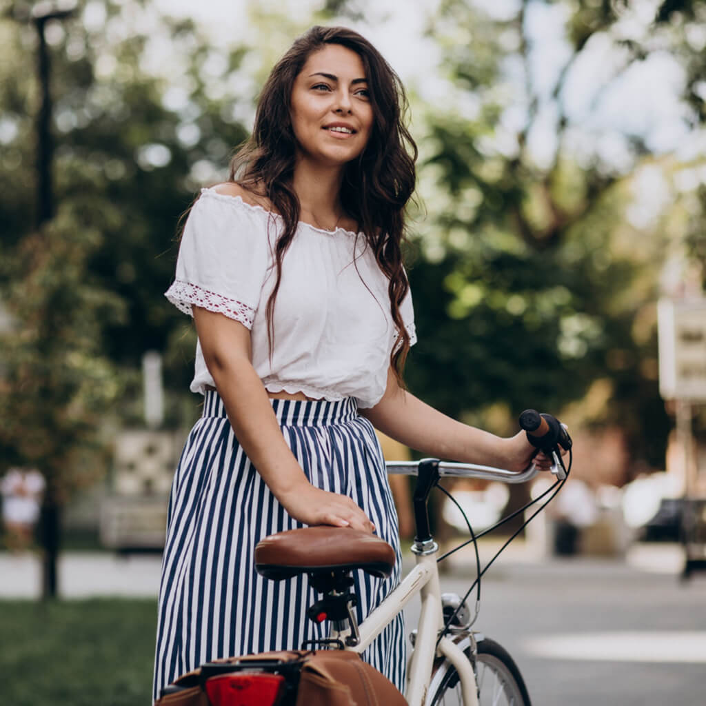 Femme souriante en tenue décontractée avec un vélo dans un parc ensoleillé.
